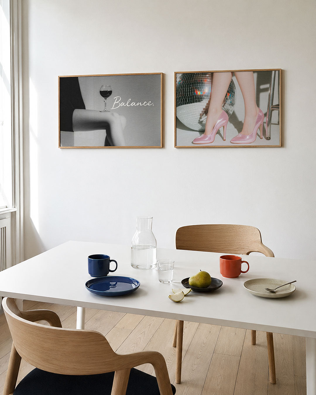 Twee liggende posters met een glas wijn op een knie in zachte grijstinten, aan de muur in een interieur